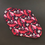 The patterned side of this cloth menstrual liner features cute skulls and death's head moths, all in shades of red, white and black. Dark red  moons and clouds swirl in the background.