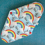This menstrual pad features rainbows on clouds and the script message "Fuck this Shit" on a sky blue background. The snaps are red, and a small tag indicates that this is a heavy absorbancy pad.