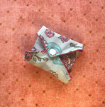 The reusable menstrual pad has been folded into a small bundle and held shut with the snap. The snap side is facing the viewer